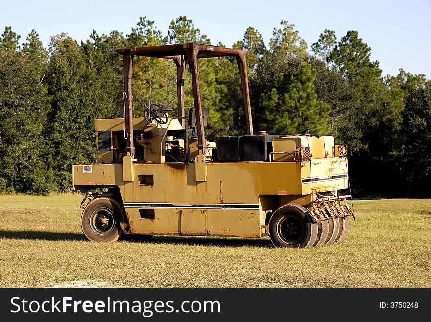A bright yellow hay rolling machine sitting in an empty field. A bright yellow hay rolling machine sitting in an empty field