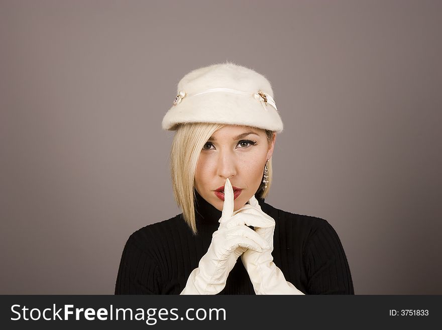 A blonde fashion model in white hat and gloves saying hush. A blonde fashion model in white hat and gloves saying hush