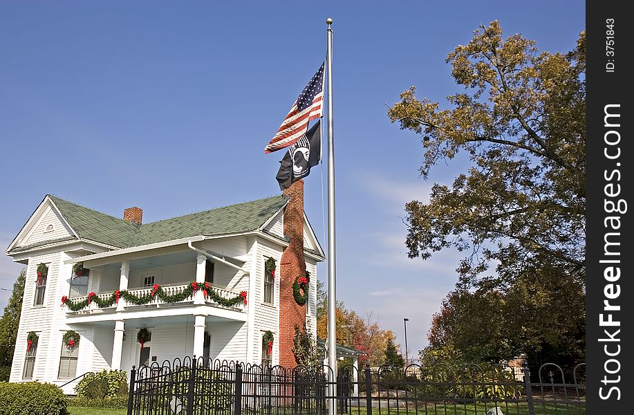 An old white colonial home decorated for Christmas with American flag and POW flag in front. An old white colonial home decorated for Christmas with American flag and POW flag in front