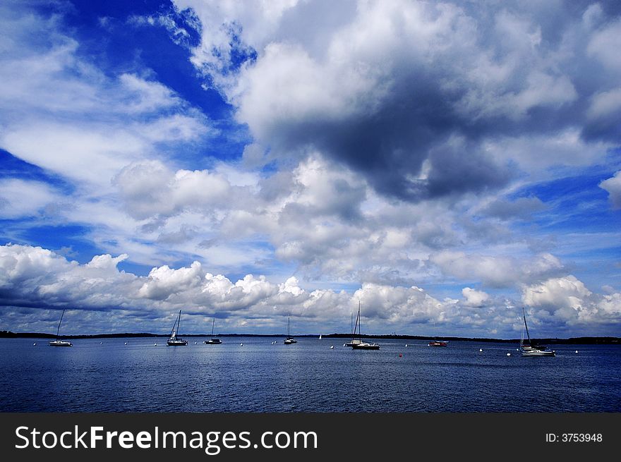 Dock floating in blue lake with sky and sailboats. Dock floating in blue lake with sky and sailboats