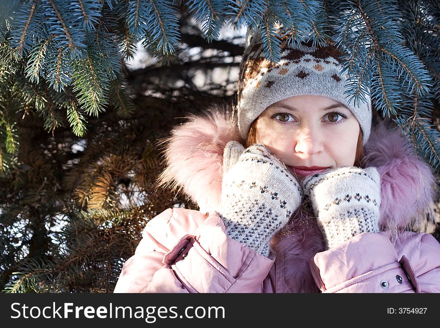 Beautiful girl in hat and mittens in snow-covered evergreens and rays of sun. Beautiful girl in hat and mittens in snow-covered evergreens and rays of sun