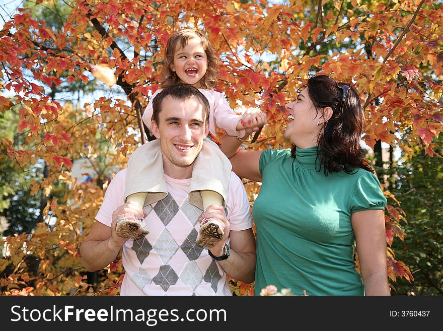 Happy baby on father`s shoulders with mother in the park