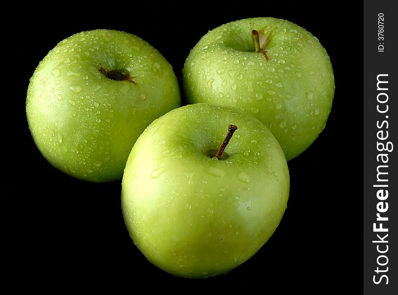 Three fresh green apples with water drops isolated on black