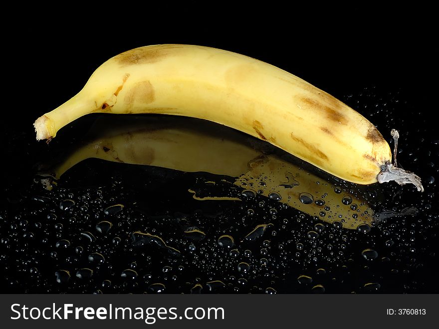 Fresh banana with water drops on wet black surface