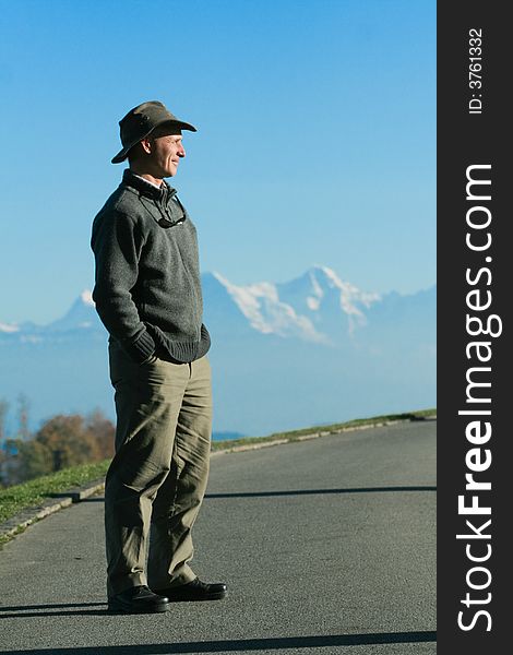 A man smiles as stands, hands in his pockets, surveying the horizon, in front of a chain of mountains in the Fall. A man smiles as stands, hands in his pockets, surveying the horizon, in front of a chain of mountains in the Fall.