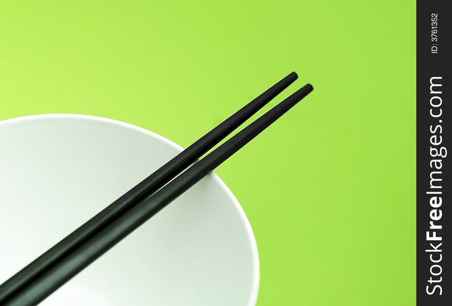 Black chopsticks on the white plate on green background