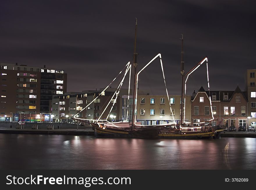 Nightscape of a river harbour in Holland with a decorated sailship in the foreground. Nightscape of a river harbour in Holland with a decorated sailship in the foreground