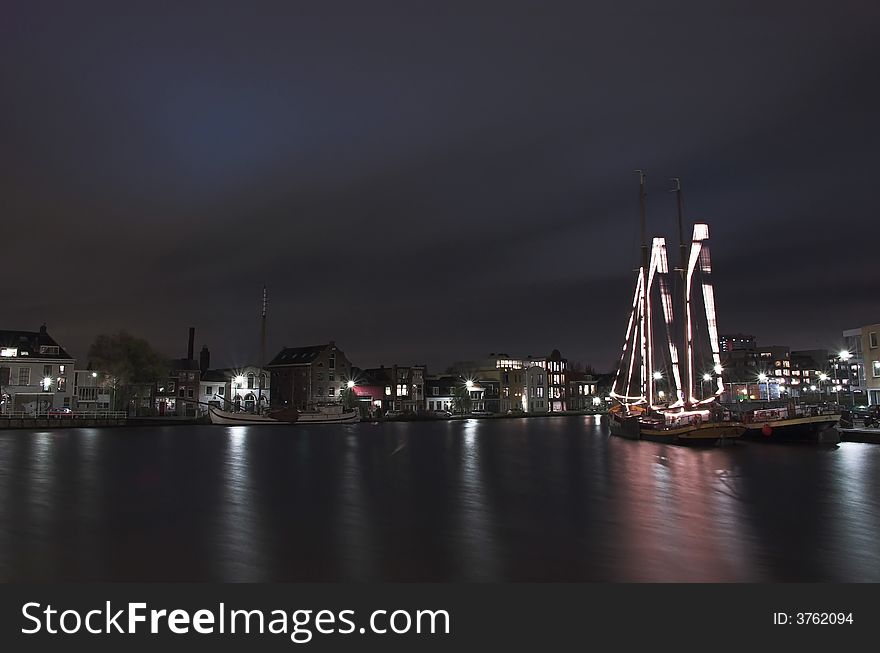 Nightscape of a river harbour in Holland with a decorated sailship in the foreground. Nightscape of a river harbour in Holland with a decorated sailship in the foreground