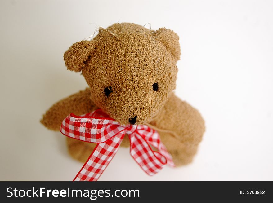 Small brown teddy bear wearing red and white gingham bow, white background. Small brown teddy bear wearing red and white gingham bow, white background