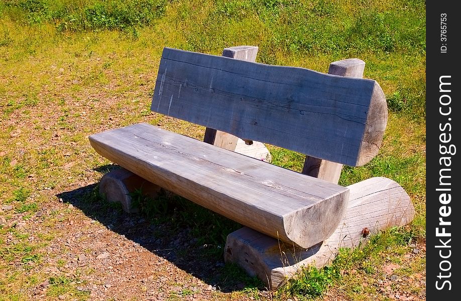 Empty grey log bench in a grassy clearing on a hot summer day.