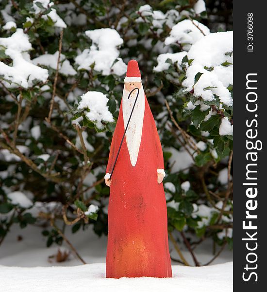 Ceramic Santa Claus figurine in the snow, in front of a green holly bush