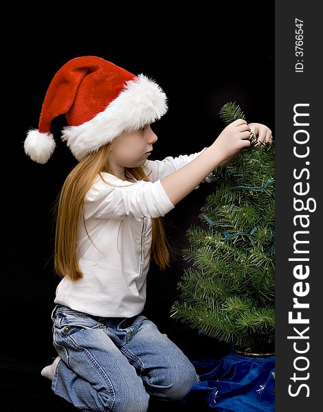 Small girl in jeans and Santa hat decorates her Christmas tree. Small girl in jeans and Santa hat decorates her Christmas tree.