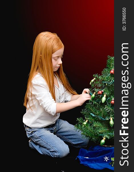 A small red haired girl decorates a miniature tree - black to red gradient background. A small red haired girl decorates a miniature tree - black to red gradient background.