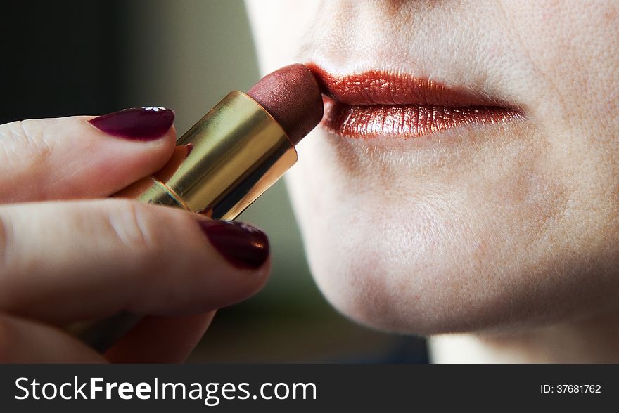 Woman paints lips with lipstick closeup