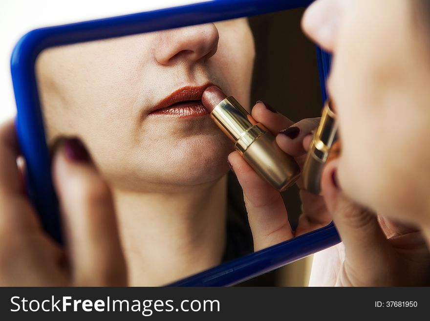 Woman paints lips with lipstick before a mirror closeup