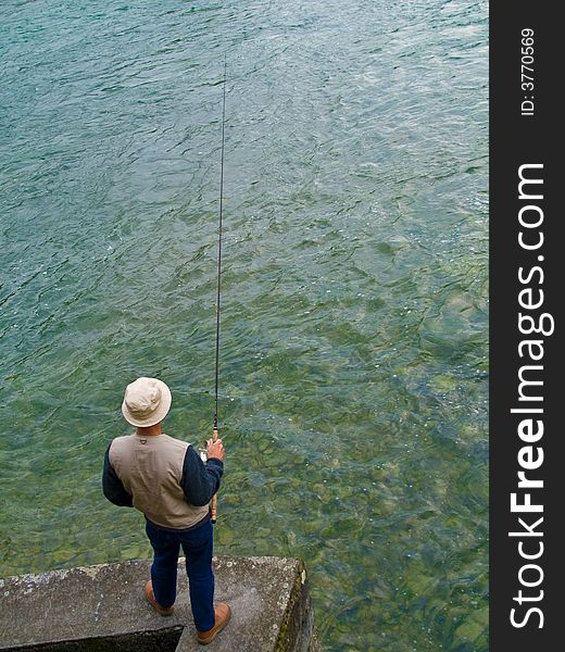 Fly fisher with a rod standing at the riverside. Fly fisher with a rod standing at the riverside