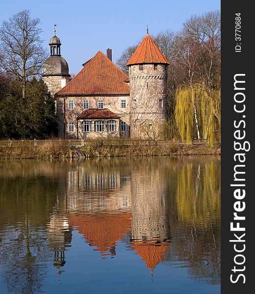 German water castle in bright sunlight 
mirroring in the lake