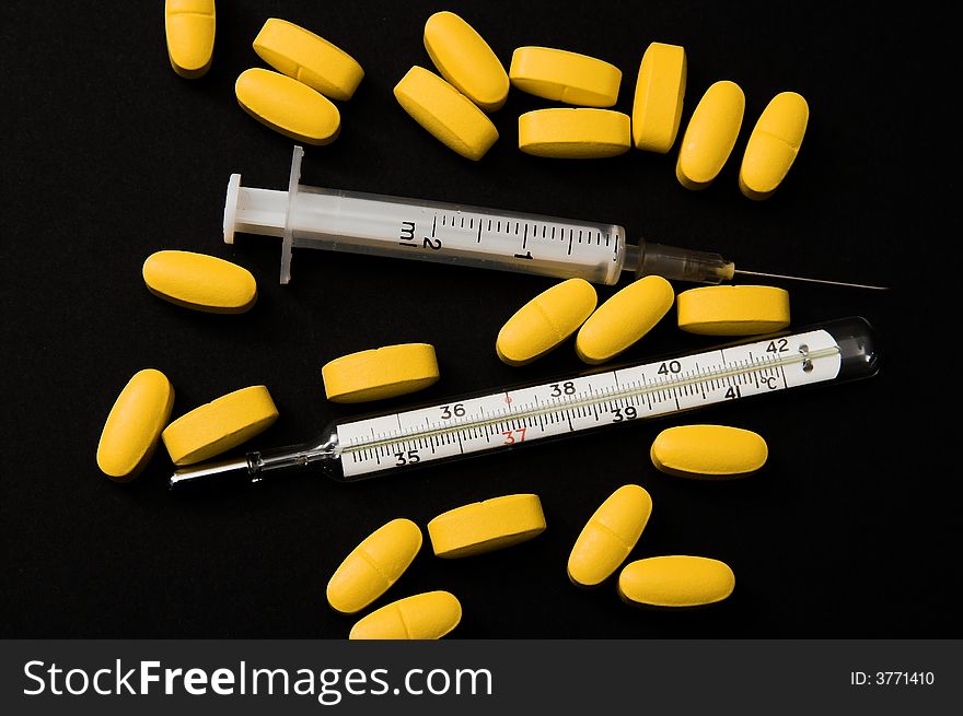 Yellow pills, syringe and thermometer (black background)