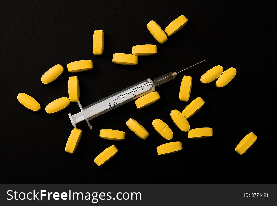 Yellow pills and syringe (black background)