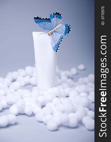 White cosmetic tube with blank area with blue butterfly on blue-gray background in artificial snow. White cosmetic tube with blank area with blue butterfly on blue-gray background in artificial snow