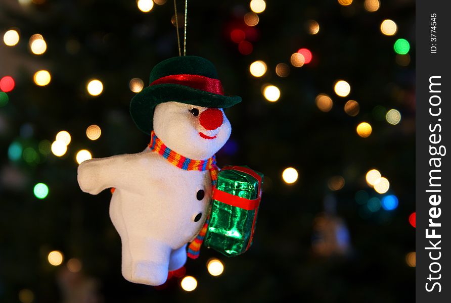 A Frosty the Snowman ornament hangs against a background of shimmering Christmas tree lights. A Frosty the Snowman ornament hangs against a background of shimmering Christmas tree lights