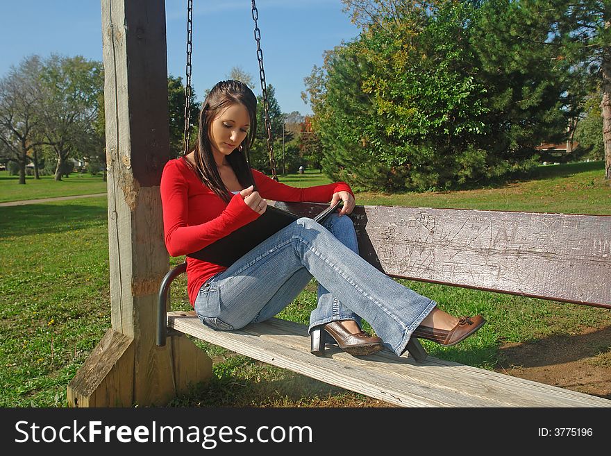 A picture of a woman reading on a bench swing in the park. A picture of a woman reading on a bench swing in the park