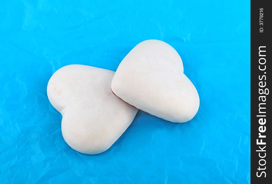 Couple of white honey-cakes hearts over blue paper. Couple of white honey-cakes hearts over blue paper