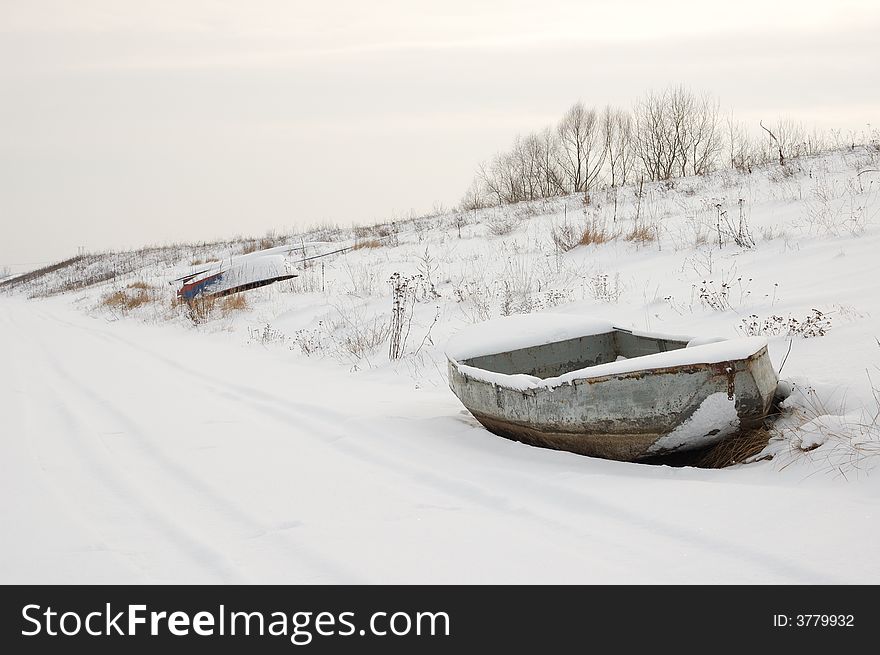 Boat on shore in snow, near road. Boat on shore in snow, near road