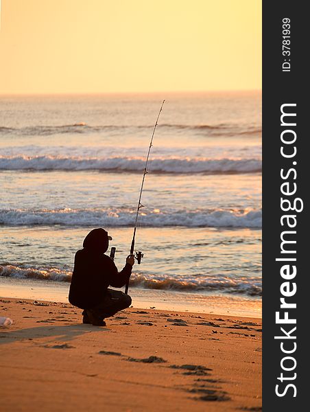 A fisherman, kneeling down surf fishing on a beautiful colorful Summer morning at sunrise. A fisherman, kneeling down surf fishing on a beautiful colorful Summer morning at sunrise.