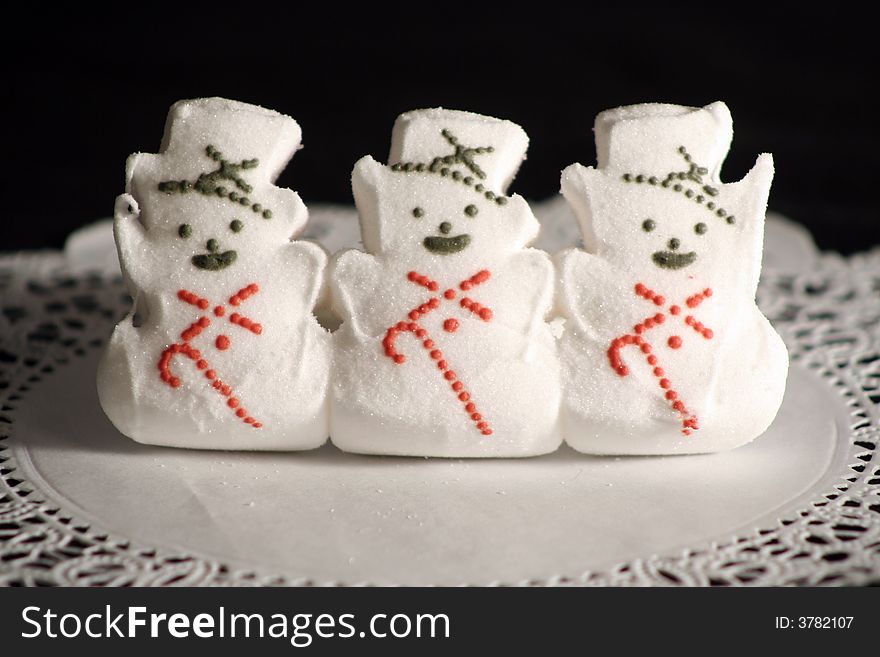 Three Marshmellow Snowmen candies on a white paper doily. Three Marshmellow Snowmen candies on a white paper doily.
