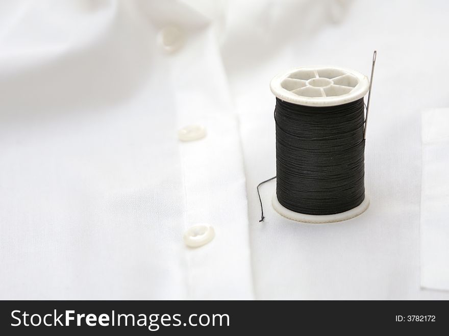 Spool of black thread on white shirt with needle. Spool of black thread on white shirt with needle