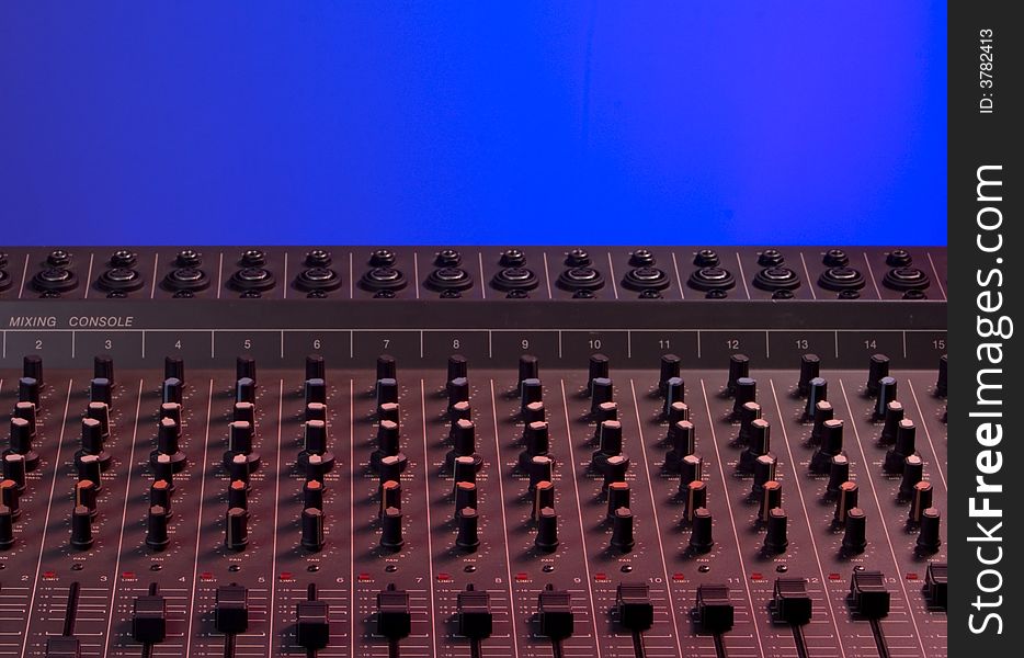 Audio mixing console dramatically lit with red light on blue background. Audio mixing console dramatically lit with red light on blue background