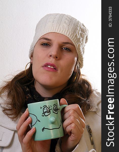 A young woman is holding a cup of tea. She is sick and in pain with winter gear on. Isolated over white with space for text. A young woman is holding a cup of tea. She is sick and in pain with winter gear on. Isolated over white with space for text.