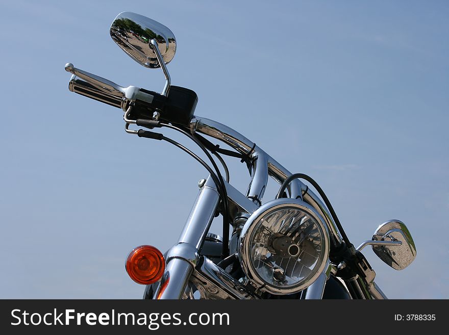 Handlebars and headlight on a chrome custom motorcycle. Handlebars and headlight on a chrome custom motorcycle