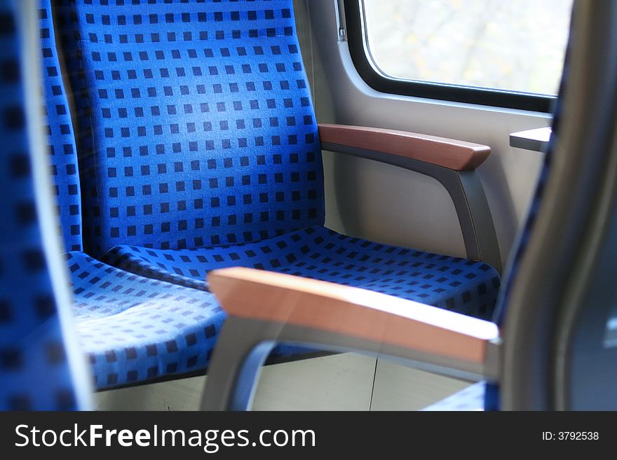 Blue train seats with wooden armrest and sun shining through the window.