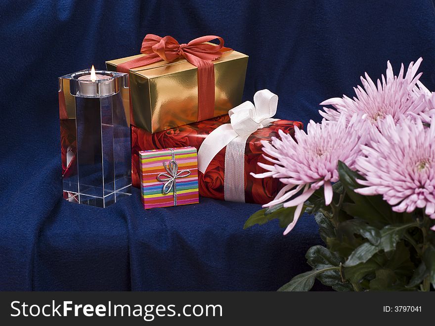 Gifts and burning candle behind flowers. Gifts and burning candle behind flowers