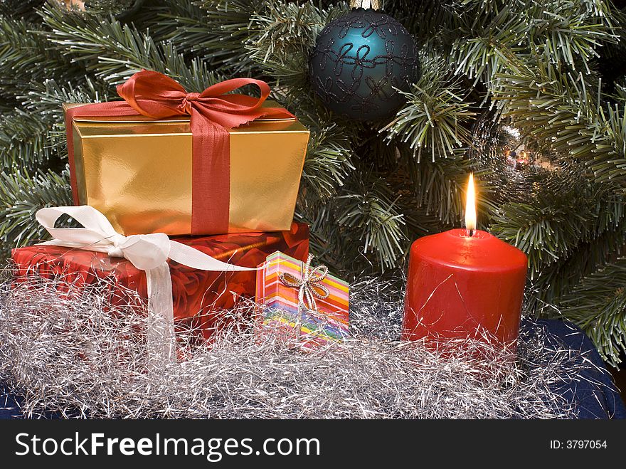 Gifts and burning candle under a Christmas tree. Gifts and burning candle under a Christmas tree