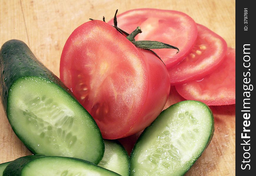 Slices of red tomato and green cucumber with waterdrops on wooden plate. Slices of red tomato and green cucumber with waterdrops on wooden plate