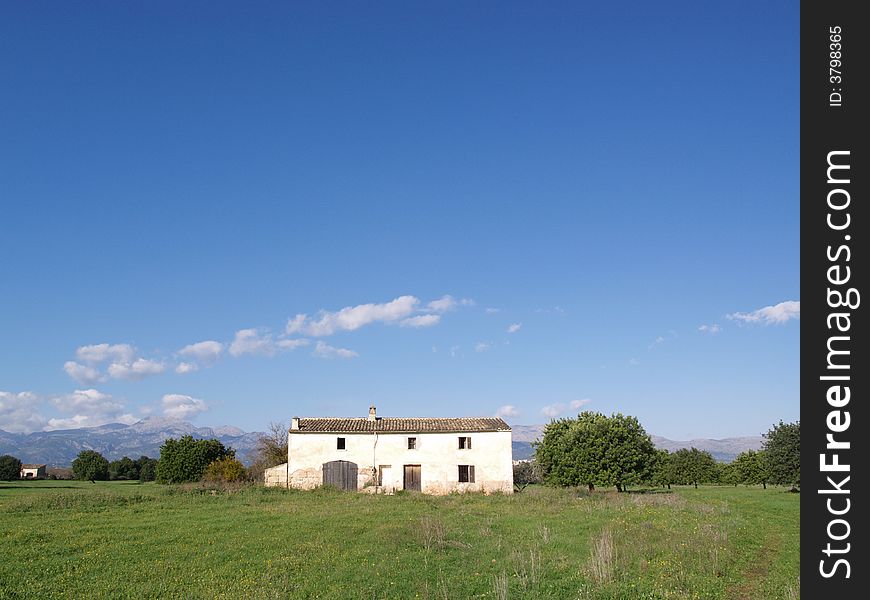 An abandoned farmhouse in the middle of a green field with mountains at the far background. An abandoned farmhouse in the middle of a green field with mountains at the far background