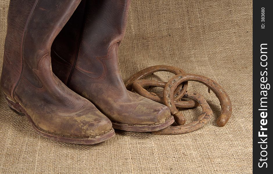 Muddy cowboy boots and old horseshoes on a burlap background. Muddy cowboy boots and old horseshoes on a burlap background.
