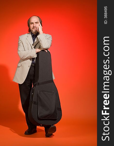 Middle aged man-musician with his guitar carrying case on a red background.