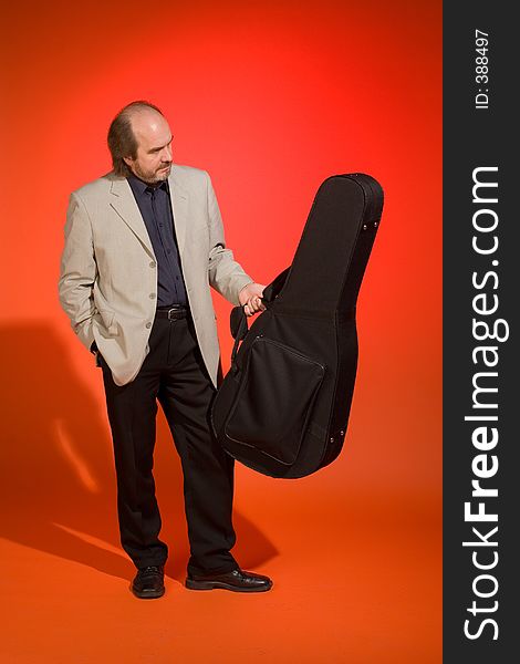 Middle aged thoughtful man-musician with his guitar carrying case on a red background. Middle aged thoughtful man-musician with his guitar carrying case on a red background.