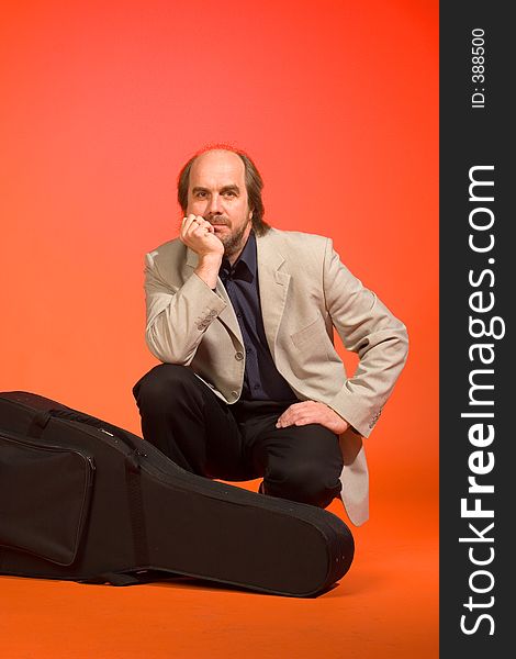 Middle aged thoughtful man-musician with his guitar carrying case on a red background. Middle aged thoughtful man-musician with his guitar carrying case on a red background.