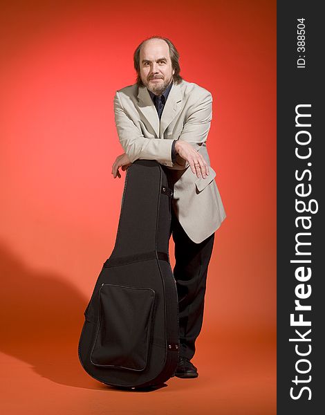 A happy looking middle aged man-musician with his guitar carrying case on a red background. A happy looking middle aged man-musician with his guitar carrying case on a red background.