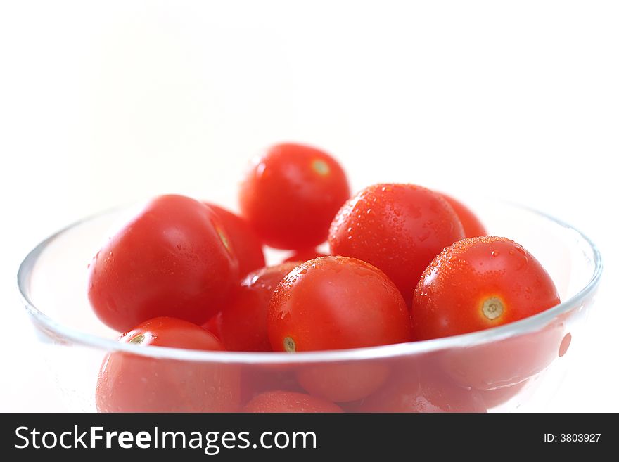 Cherry tomatoes in a transparent glass bowl on a white table-top