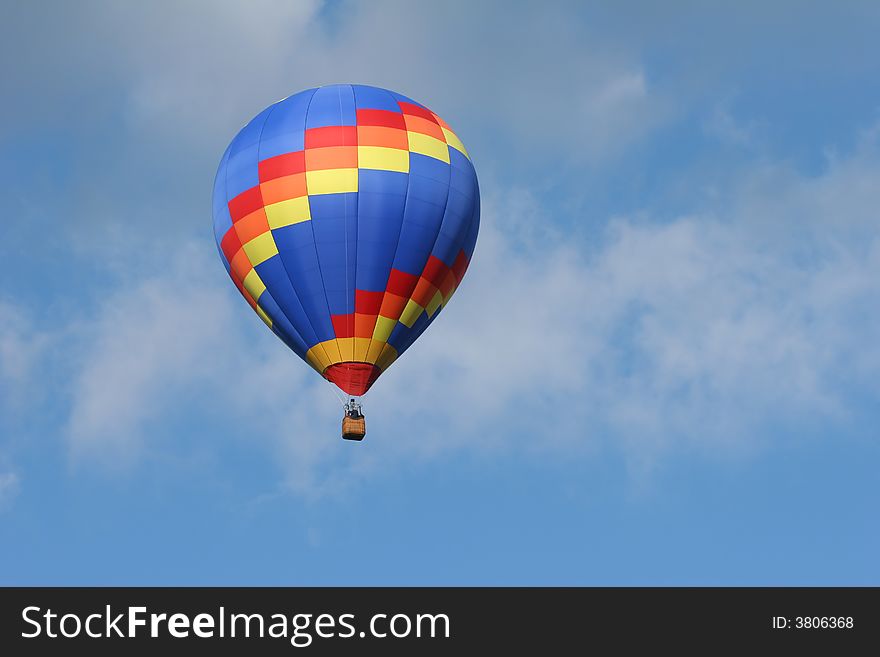 One multi colored hot air ballon with a cloudy blue sky. One multi colored hot air ballon with a cloudy blue sky