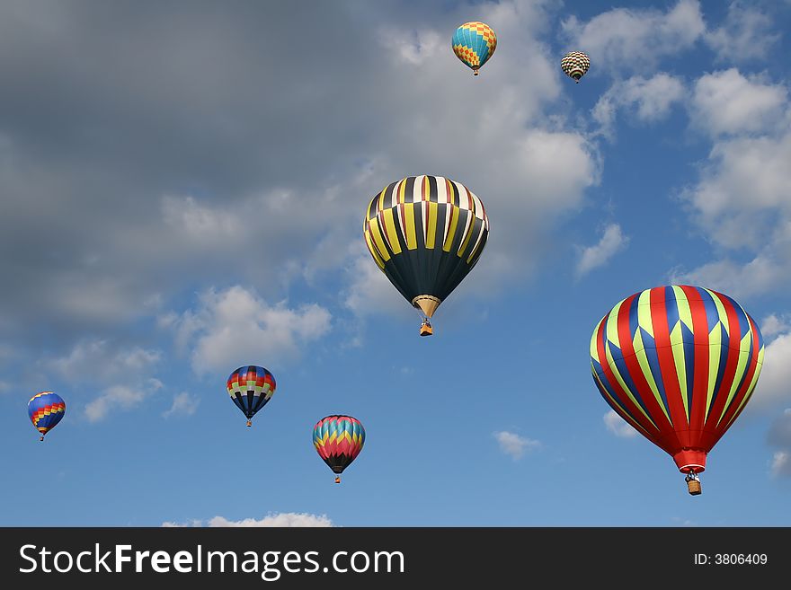 Seven hot air balloons flying in a cloudy blue sky