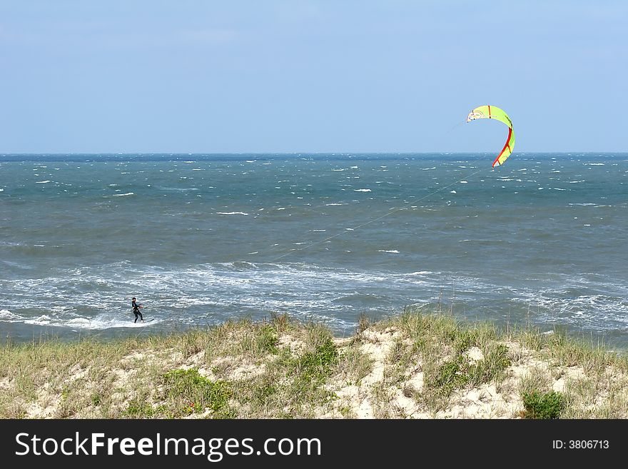 A Kite Surfer in the ocean with a sand dune in front