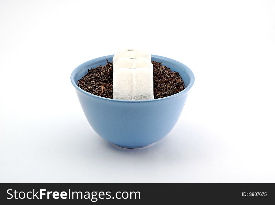 Tea leafs and bags in blue bowl on white background