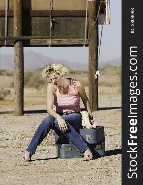 Unhappy blonde woman sitting on suitcases in a remote location